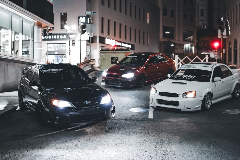 Three modified cars parked on an urban street at night